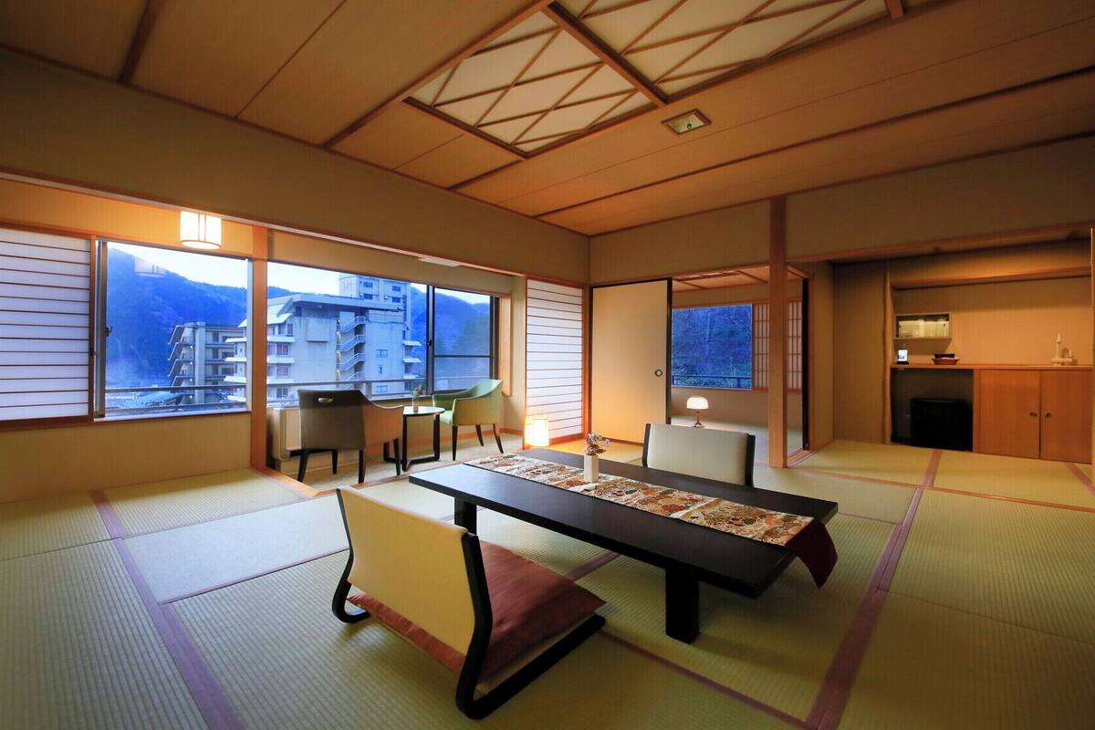 Una habitación japonesa tradicional con suelo de tatami, una mesa baja, una silla y una puerta corrediza que da a una zona de cocina.