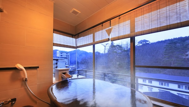 Un onsen japonés tradicional con un extenso manantial termal, vista a la montaña y ventana con vistas a edificios.
