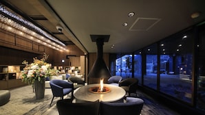 Un área de estar interior moderna con una mesa redonda, sillas, un jarrón grande con flores y una chimenea decorativa.