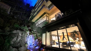 Un edificio moderno con fachada de vidrio, zona de estar al aire libre y una formación rocosa con iluminación de colores.