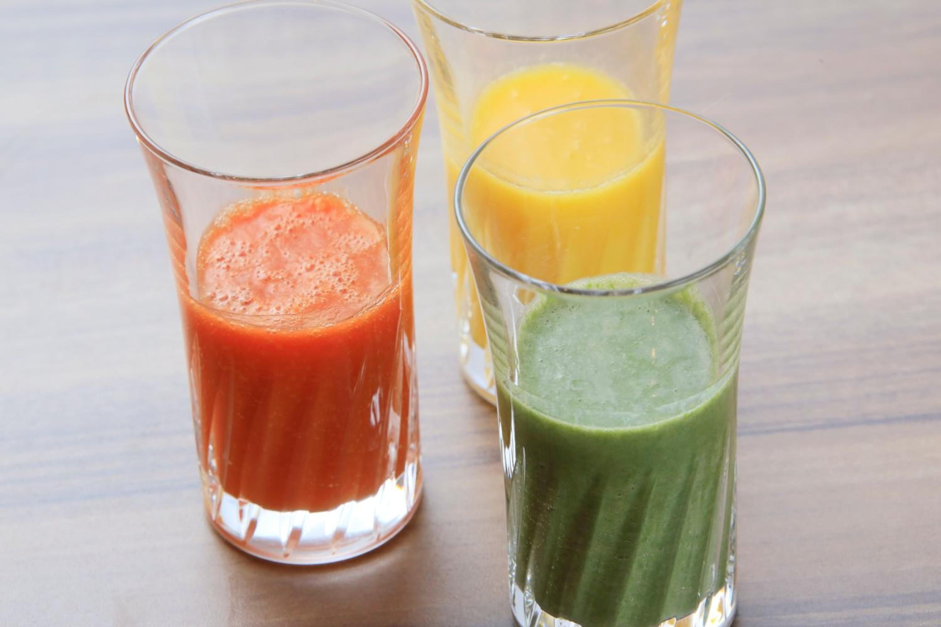 Three glasses of different colored smoothies on a wooden surface.