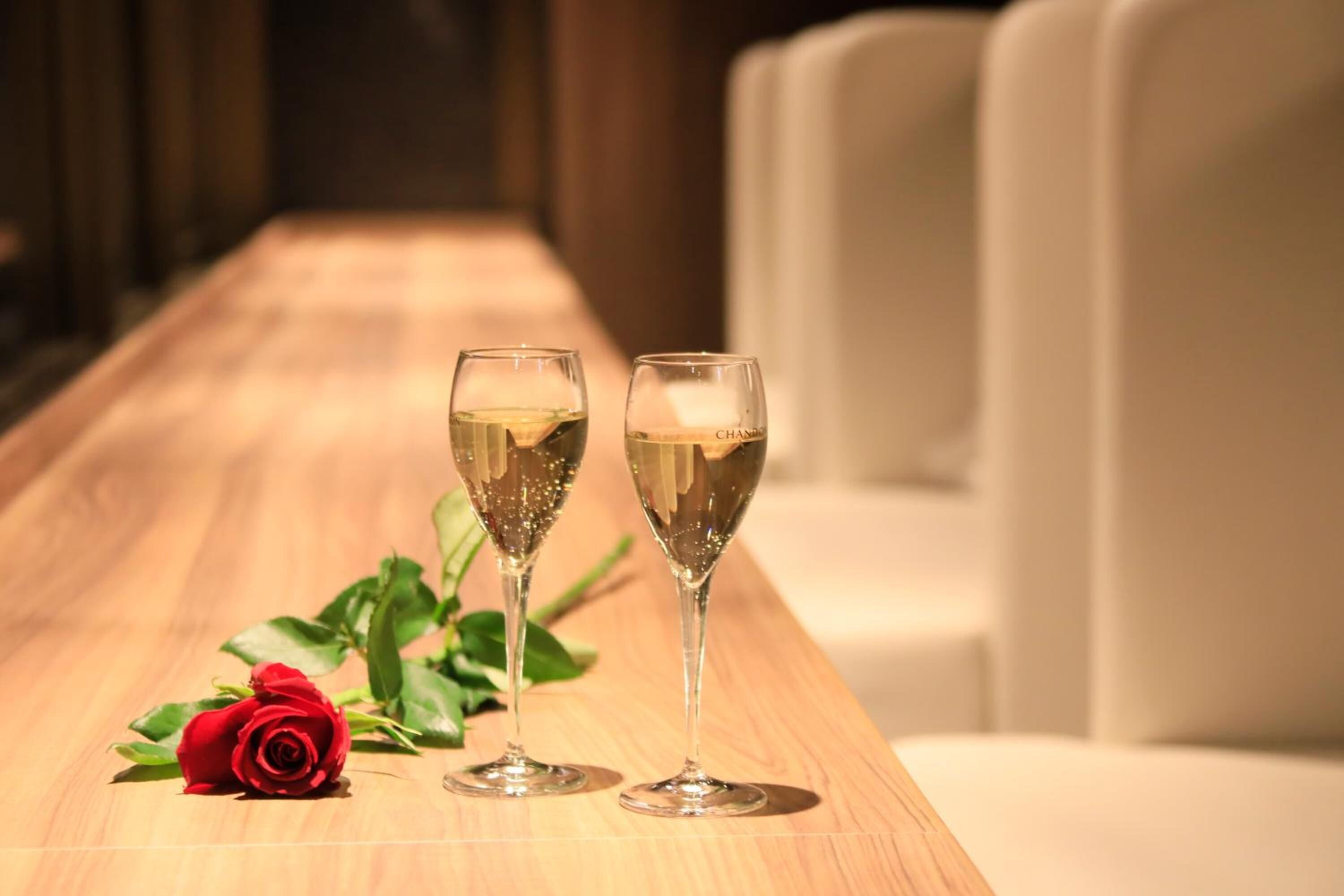 Dos copas de champán sobre una mesa de madera con una rosa roja a un lado.