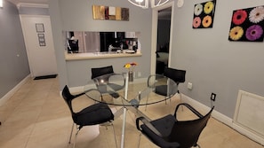 Een moderne eetruimte met een glazen tafel, omringd door zwarte stoelen, een vaas met bloemen en een keuken op de achtergrond.