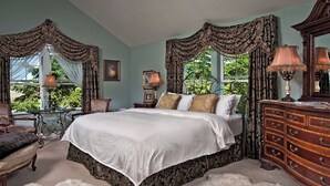 A bedroom with a large bed, ornate curtains, a dresser, and a chair.