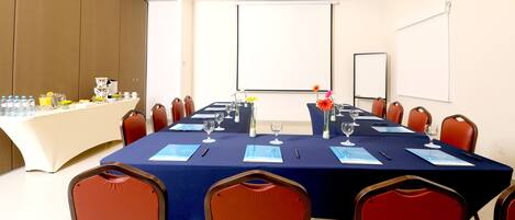 Una sala de conferencias con una larga mesa, sillas y una pantalla para proyector.