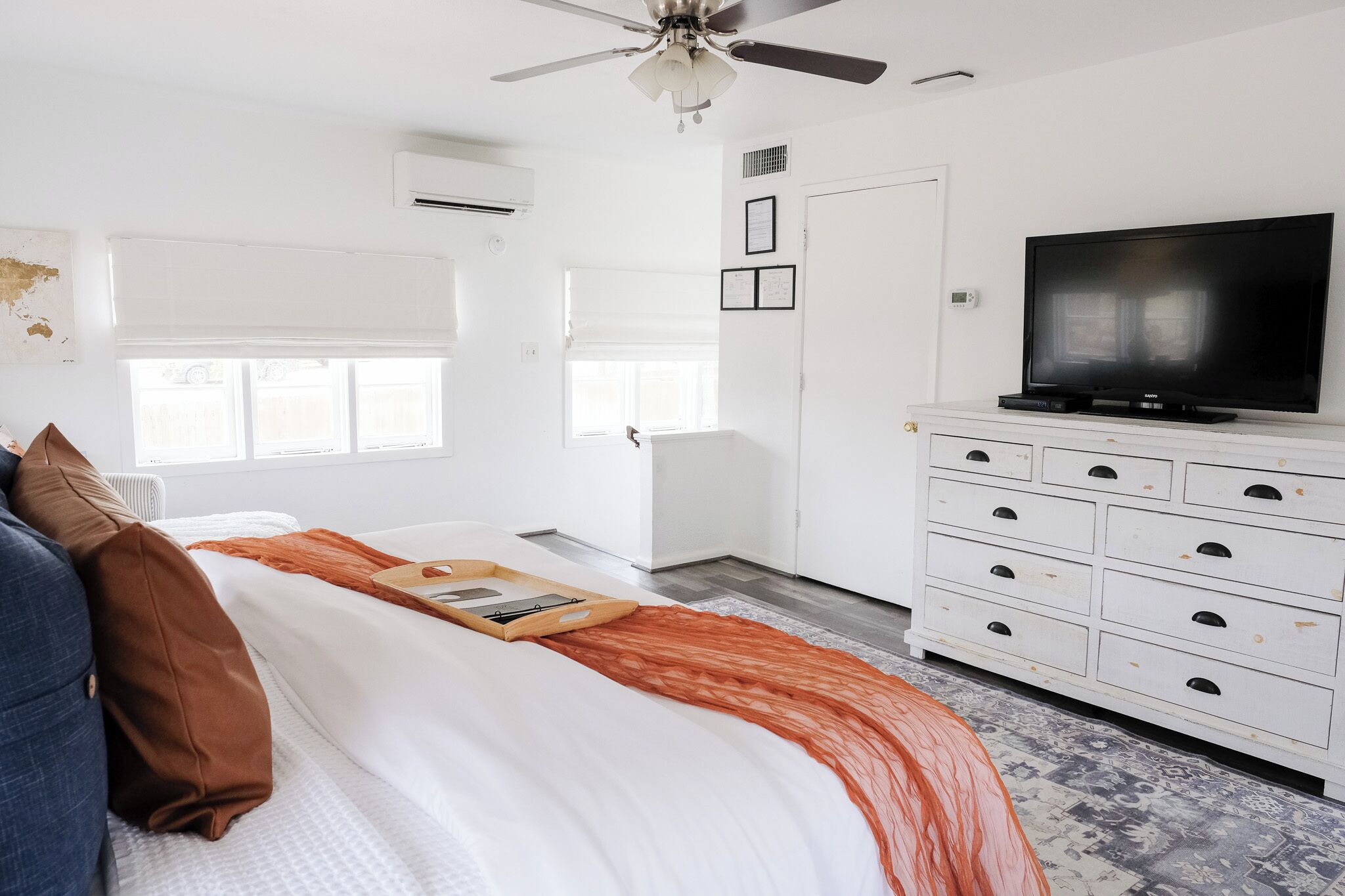 A bedroom with a bed, a TV, a dresser, and a ceiling fan.