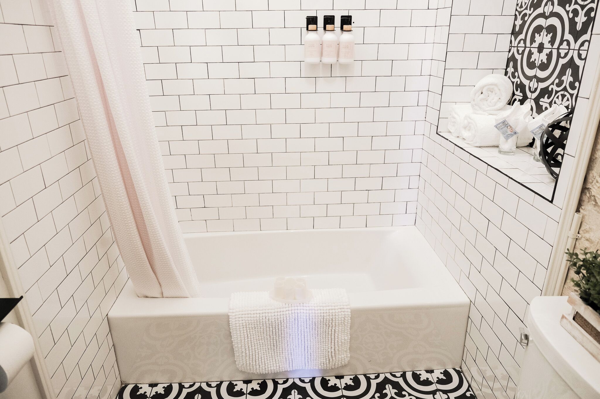 Un bagno con pareti rivestite di piastrelle bianche, una vasca da bagno bianca e un pavimento a motivi bianchi e neri.