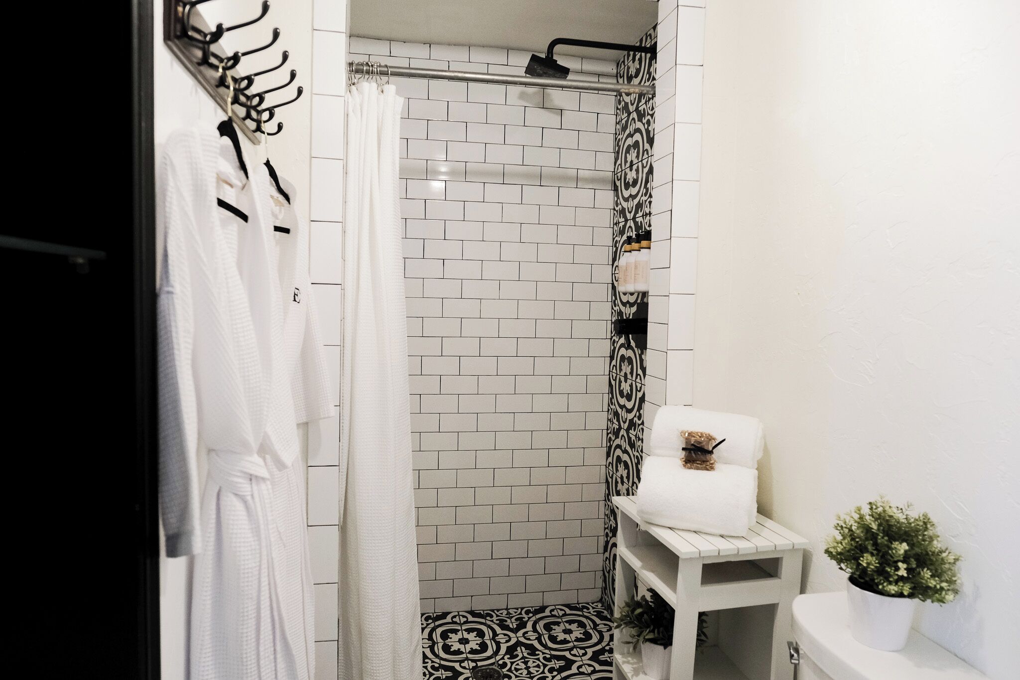 A bathroom with white tiled walls, a shower area, and a small white vanity with a potted plant.