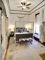 Ein Schlafzimmer mit Himmelbett, Deckenventilator, Wanddeko in Form eines Stierkopfes, Nachttisch mit Lampe und einem fenster mit Vorhängen.
