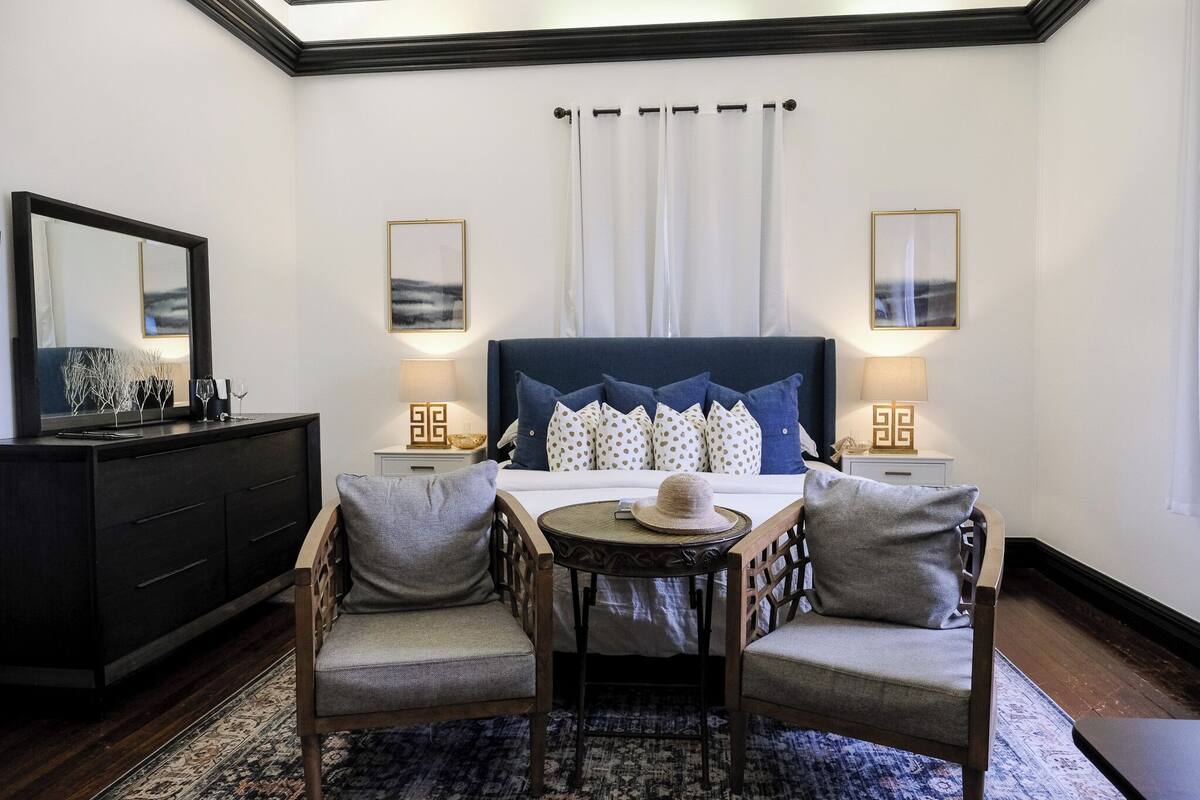 A hotel room with a large bed, two bedside tables with lamps, a dresser, and a small round table with chairs.