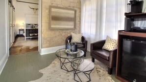 A living room with a stone wall, leather sofa, glass coffee table, and a television. - The Evers House (Fredericksburg)
