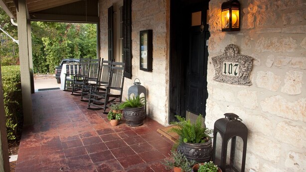 A stone building with a number plaque, a covered porch with chairs, and potted plants. - The Evers House (Fredericksburg)