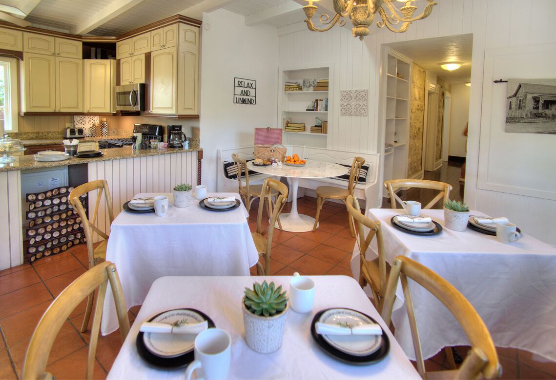 Zona pranzo con tavoli e sedie bianche, una cucina sullo sfondo e un cartello con la scritta 'RELAX AND UNWIND'.