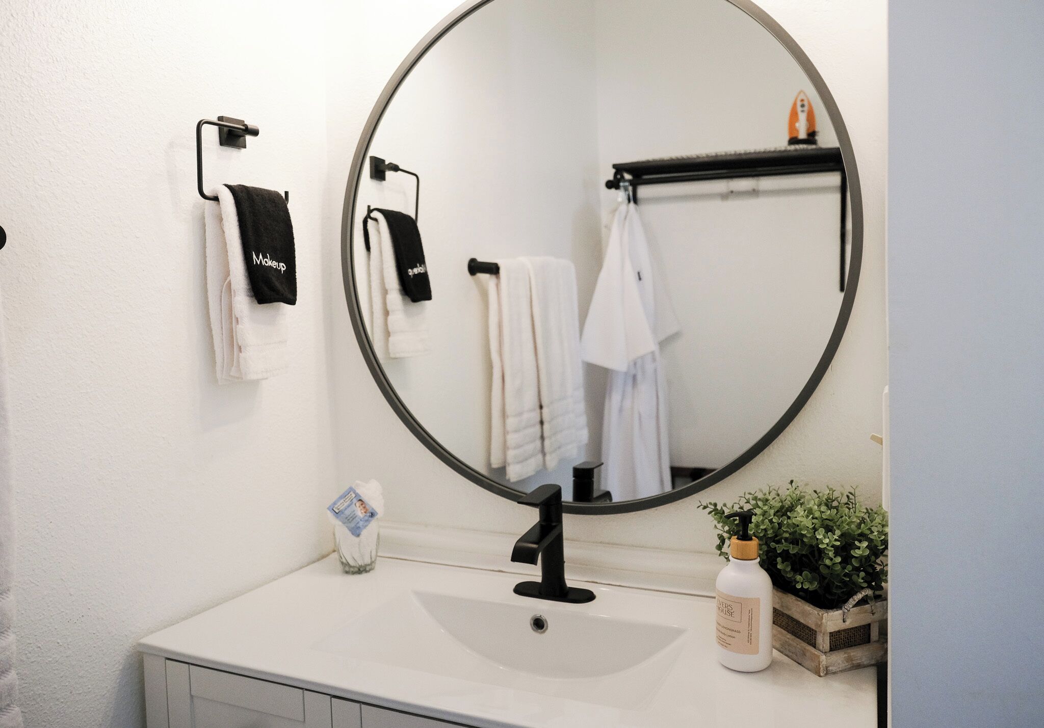 Un baño con un espejo redondo, lavabo blanco y toallero con varias toallas.