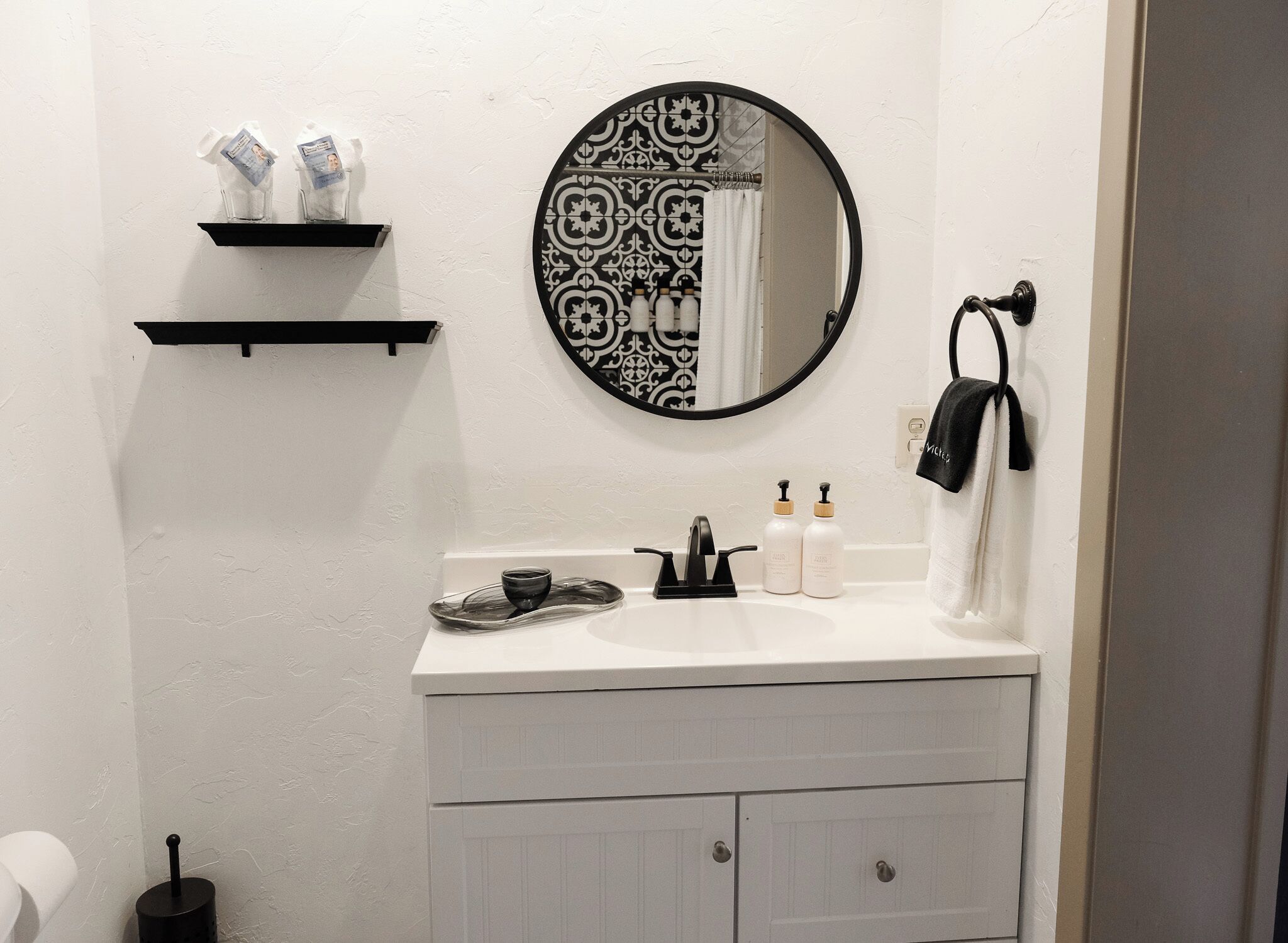 Un baño con lavamanos blanco, espejo con diseño blanco y negro, y un perchero para toallas.