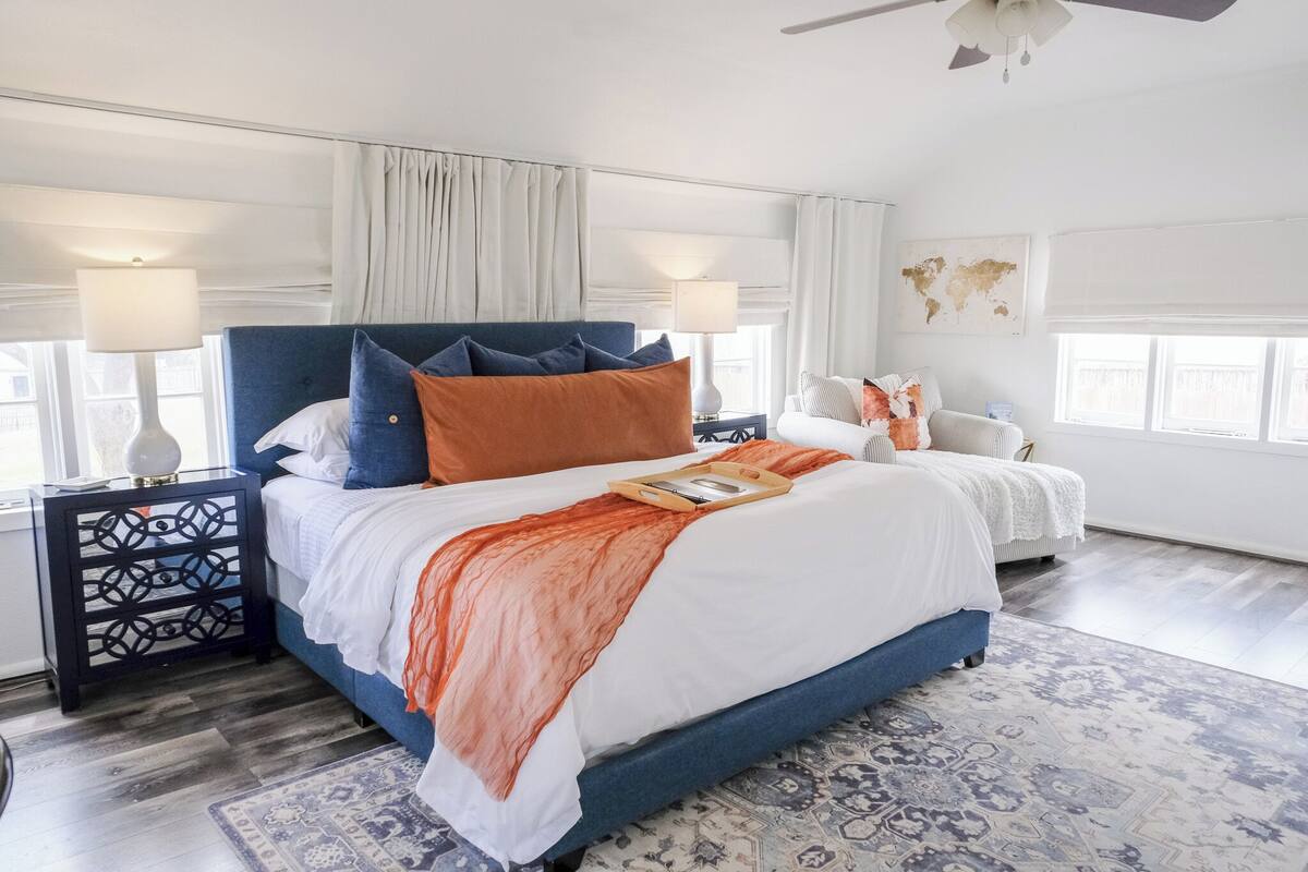 A bedroom with a large bed, two bedside tables, a nightstand, a window with curtains, and a world map on the wall.