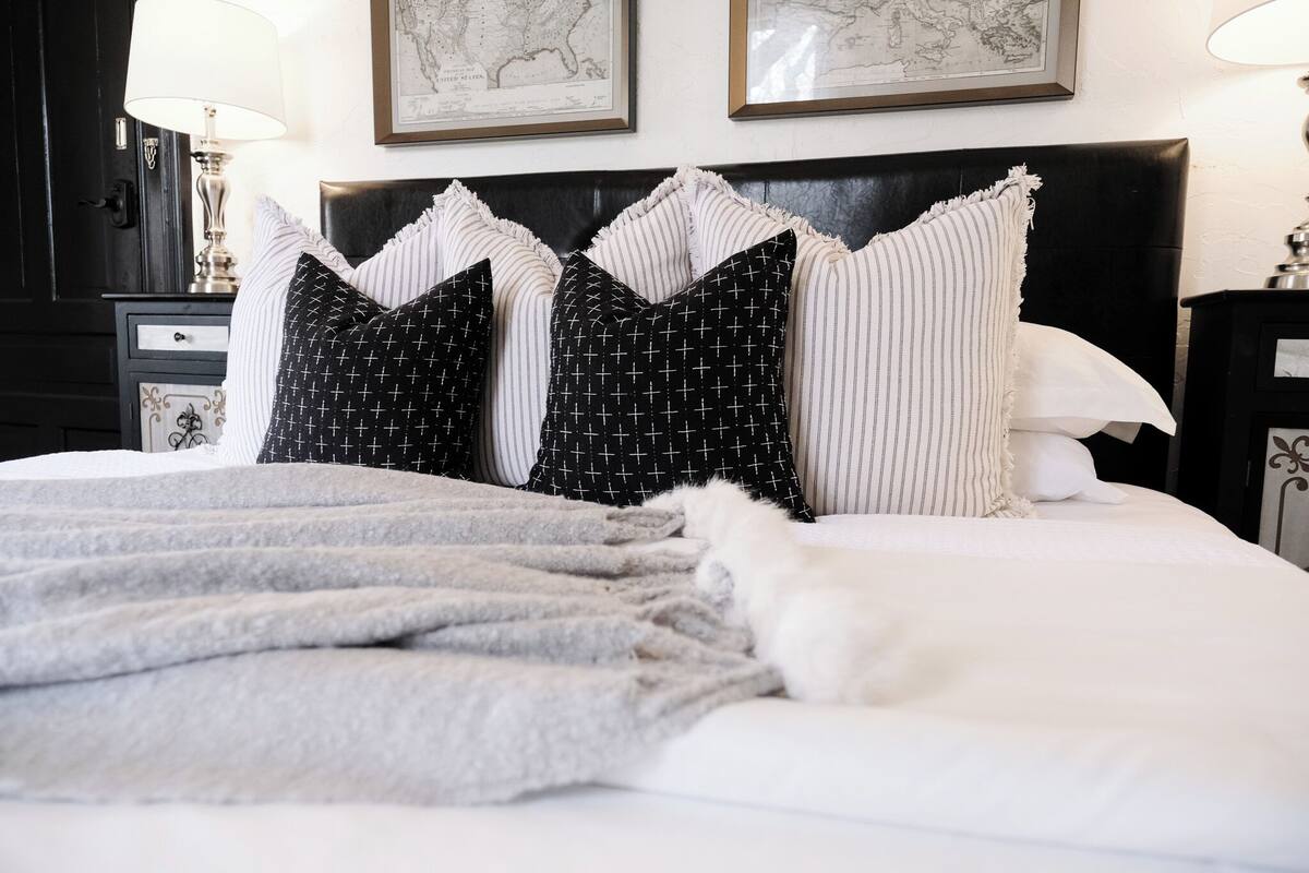 A neatly made bed with a grey blanket and multiple pillows, including black and white striped ones.