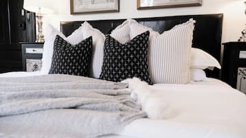 Una cama bien hecha con un edredón gris y varios almohadones, incluyendo unos a rayas blancas y negras.