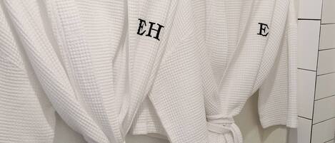 Deux robes blanches sont suspendues à un porte-serviettes noir fixé au mur, dans une salle de bain.
