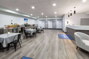 A spacious dining area with tables and chairs, a counter with a coffee station, and a reception desk. - Travelodge by Wyndham Cochrane Ontario (Cochrane)