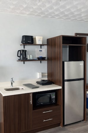 A modern kitchen with a built-in microwave, a stainless steel refrigerator, a sink, and wooden cabinets. - Travelodge by Wyndham Cochrane Ontario (Cochrane)