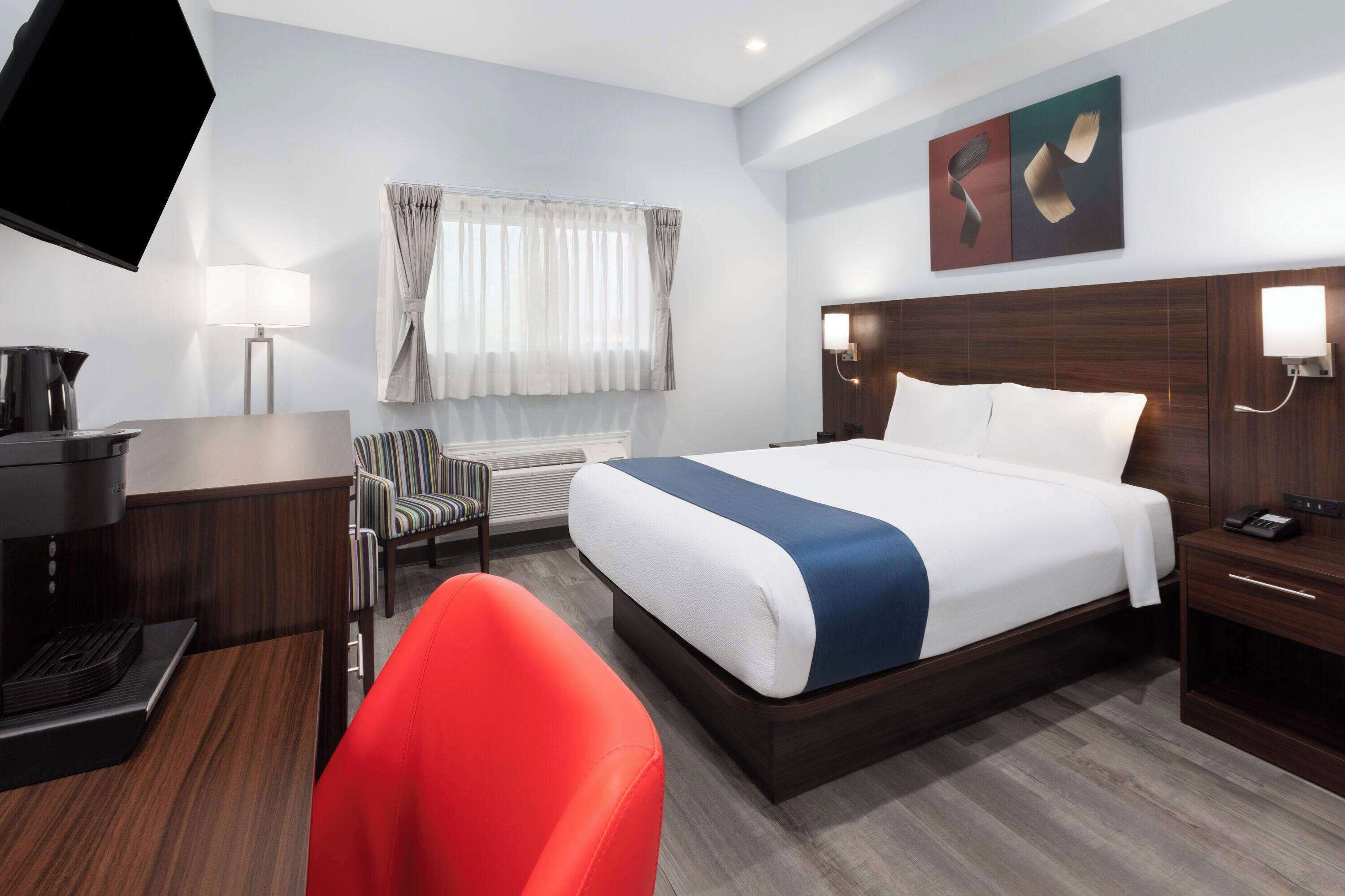 Une chambre d’hôtel avec un grand lit, un bureau avec une machine à café, une chaise et un téléviseur fixé au mur.