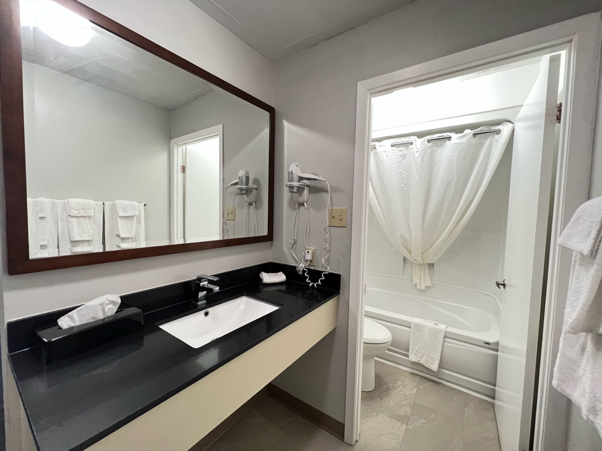 Un baño con encimera negra, lavamanos blanco, espejo, cortina de ducha y retrete.