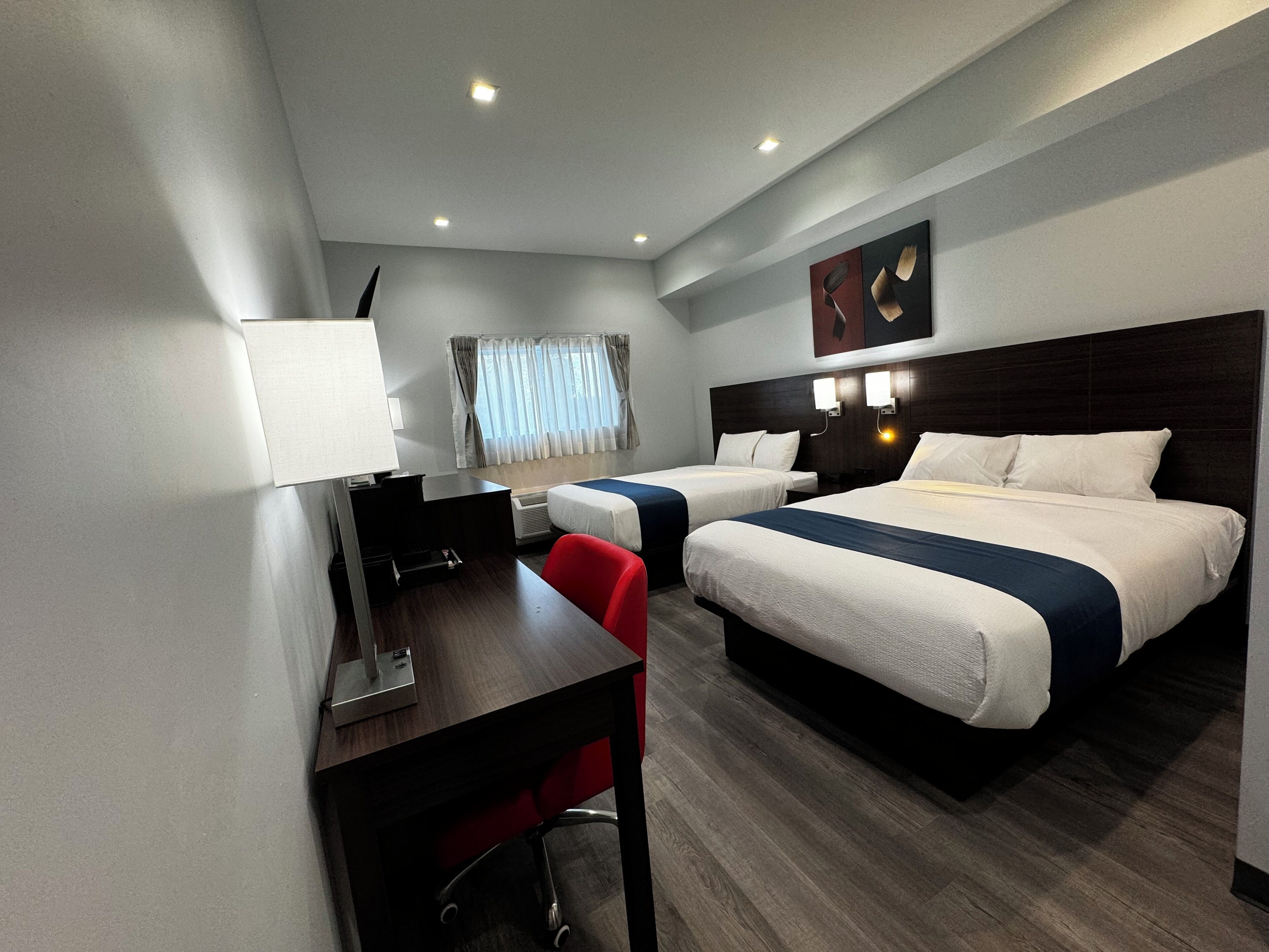 A hotel room with two beds, a desk, a chair, a TV, and a window with curtains.