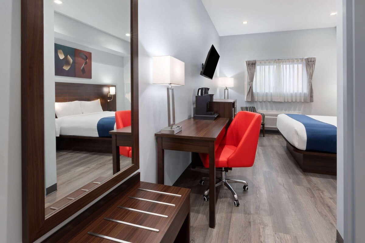A hotel room with a bed, a desk, a chair, a TV, and a window with curtains.