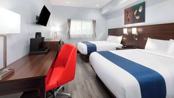 Une chambre d’hôtel avec deux lits, un bureau, une chaise rouge, un téléviseur à écran plat fixé au mur et une fenêtre avec des rideaux.