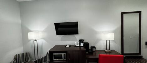Une chambre d’hôtel avec un bureau en bois foncé, une chaise rouge, un téléviseur fixé au mur et deux lampadaires.