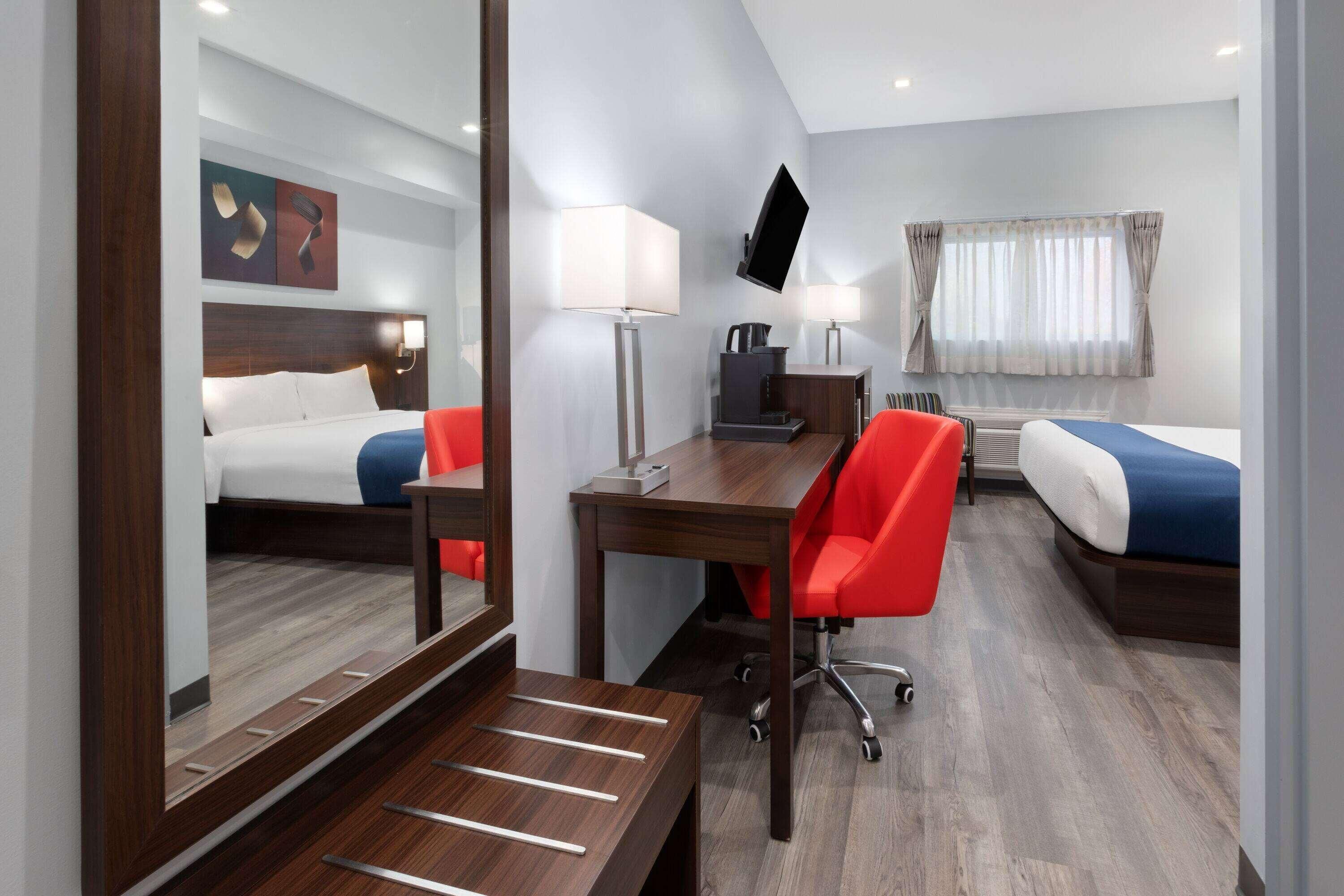A hotel room with a bed, a desk, a chair, a TV, and a window with curtains.