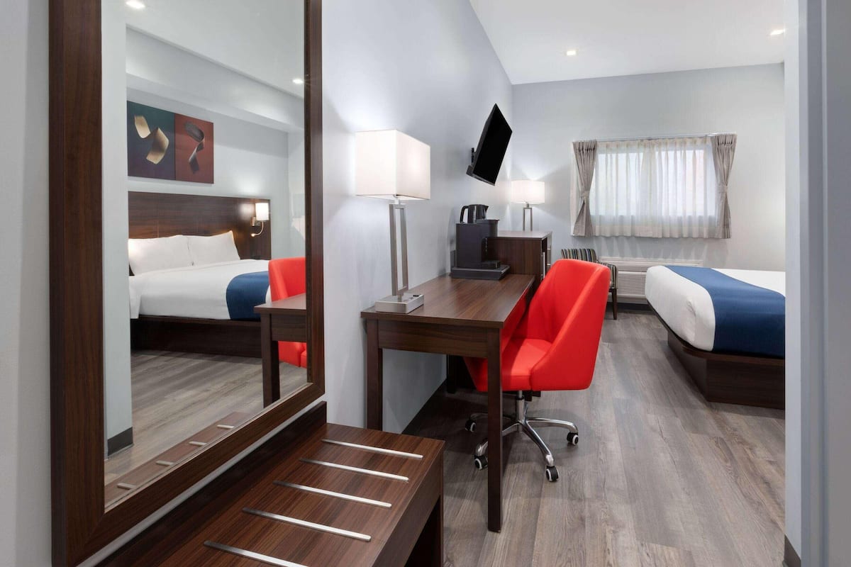 A hotel room with a bed, a desk, a chair, a TV, and a window with curtains.