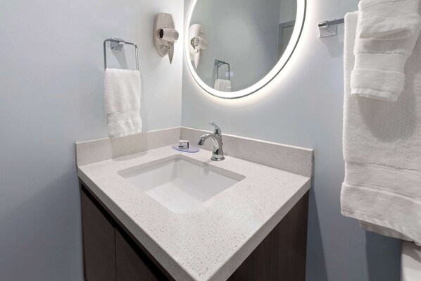 A bathroom with a white sink, a mirror, and two hair dryers mounted on the wall.