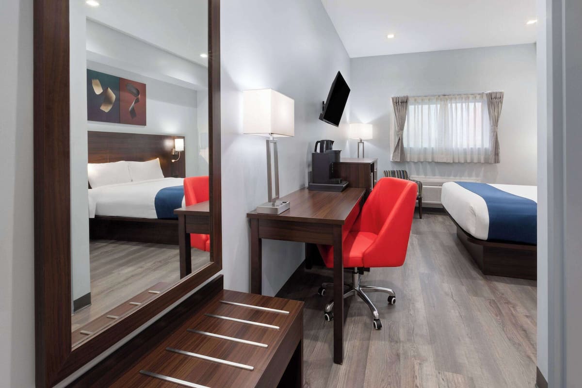 A hotel room with a wooden desk, two beds, a TV, and a large mirror.