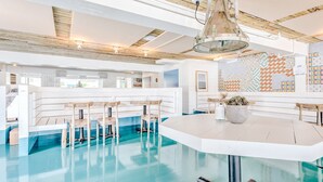 A modern bar with a pool table, bar stools, and a large potted plant. - The Surf Lodge (Montauk)