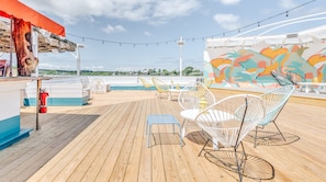 A deck with wooden flooring, white and yellow chairs, a small table, and a mural.