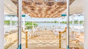 An outdoor deck with white chairs and tables, a wooden floor, and a view of a lake. - The Surf Lodge (Montauk)