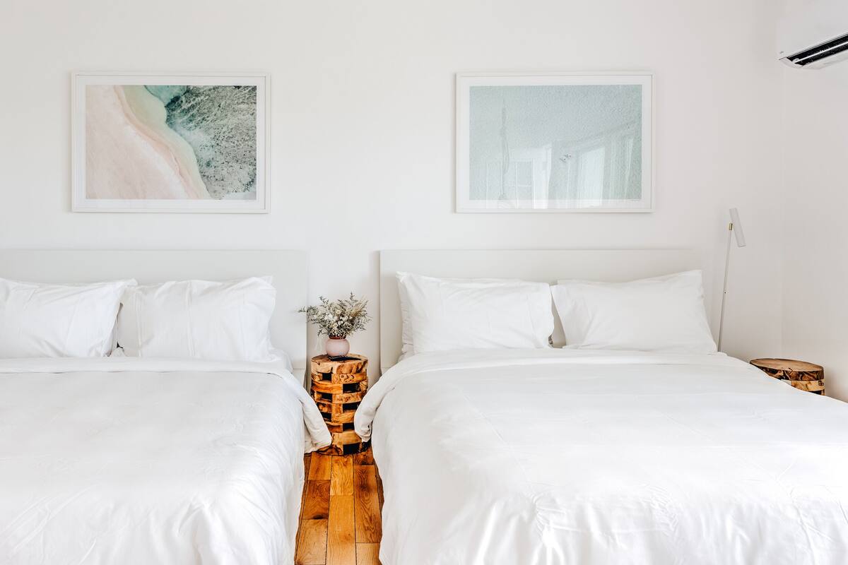 A hotel room with two beds, white bedding, a wooden floor, and two framed artworks on the walls.