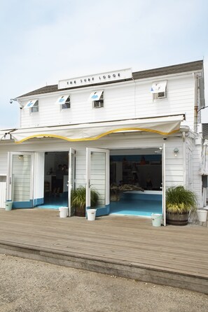 A white building with a sign reading "The Surf Lodge." It has a covered entrance with two potted plants and a wooden deck in front.