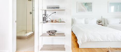 A modern bedroom with a large bed, a walk-in closet with shelves, and a shower area.