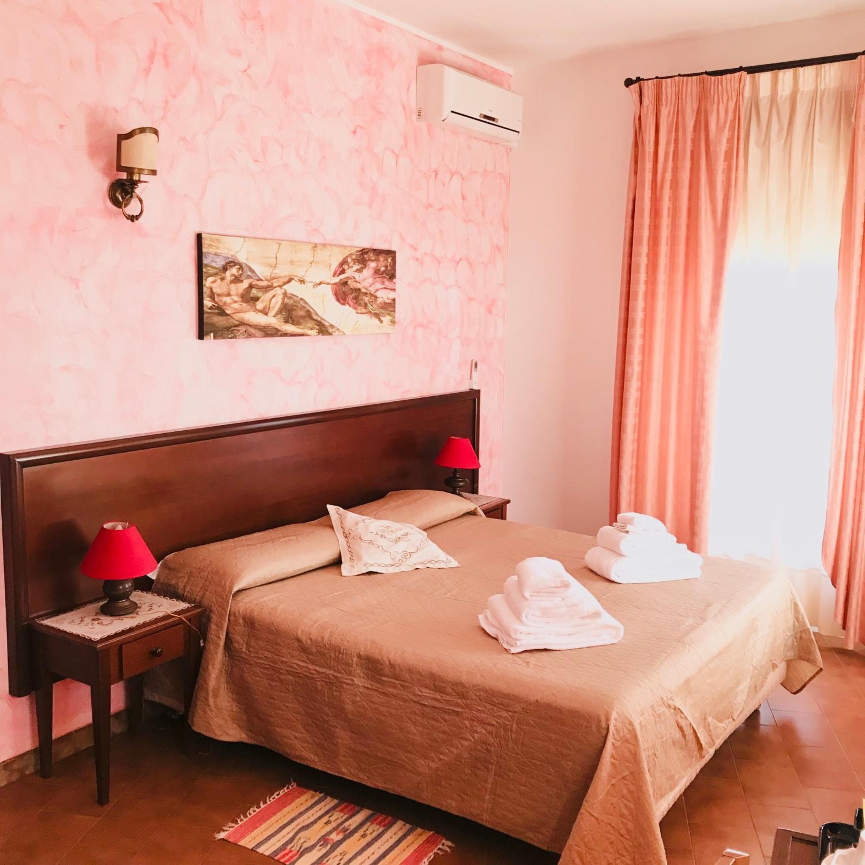 Une chambre d’hôtel avec un grand lit, deux tables de chevet avec des lampes, un tableau au mur, un appareil de climatisation et une fenêtre avec des rideaux.