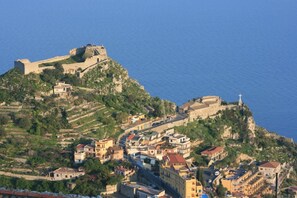 A coastal town with a prominent fortification on a hill, surrounded by residential buildings and a clear view of the sea. - Villa Regina (Castelmola)
