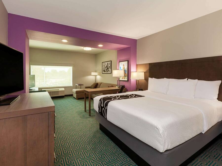 A hotel room with a large bed, a desk, a chair, a TV, and a window.