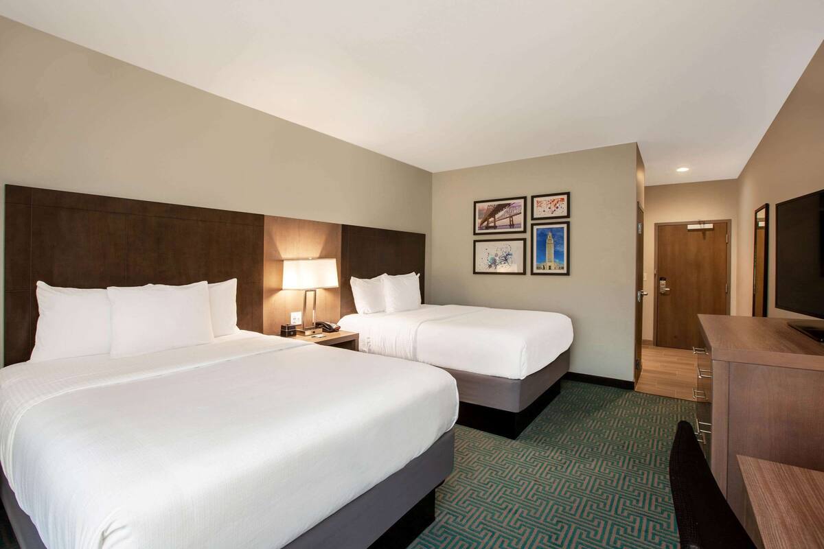 A hotel room with two beds, a desk, a chair, a TV, and a door.