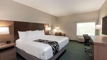 A hotel room with a large bed, bedside lamps, a desk with a chair, and a window with blinds.