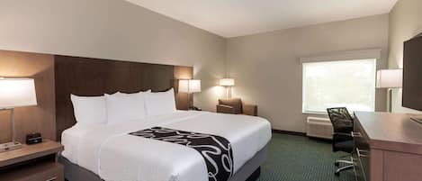 Een hotelkamer met een groot bed, nachtlampjes, een bureau met stoel en een raam met jaloezieën.