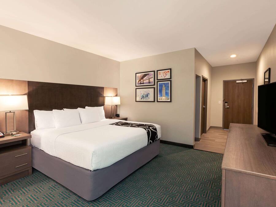 A hotel room with a bed, bedside tables, a TV, and artwork on the wall.