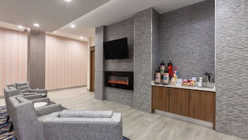 Uma sala de estar moderna com sofás cinzas, lareira, TV de tela plana e minibarra.