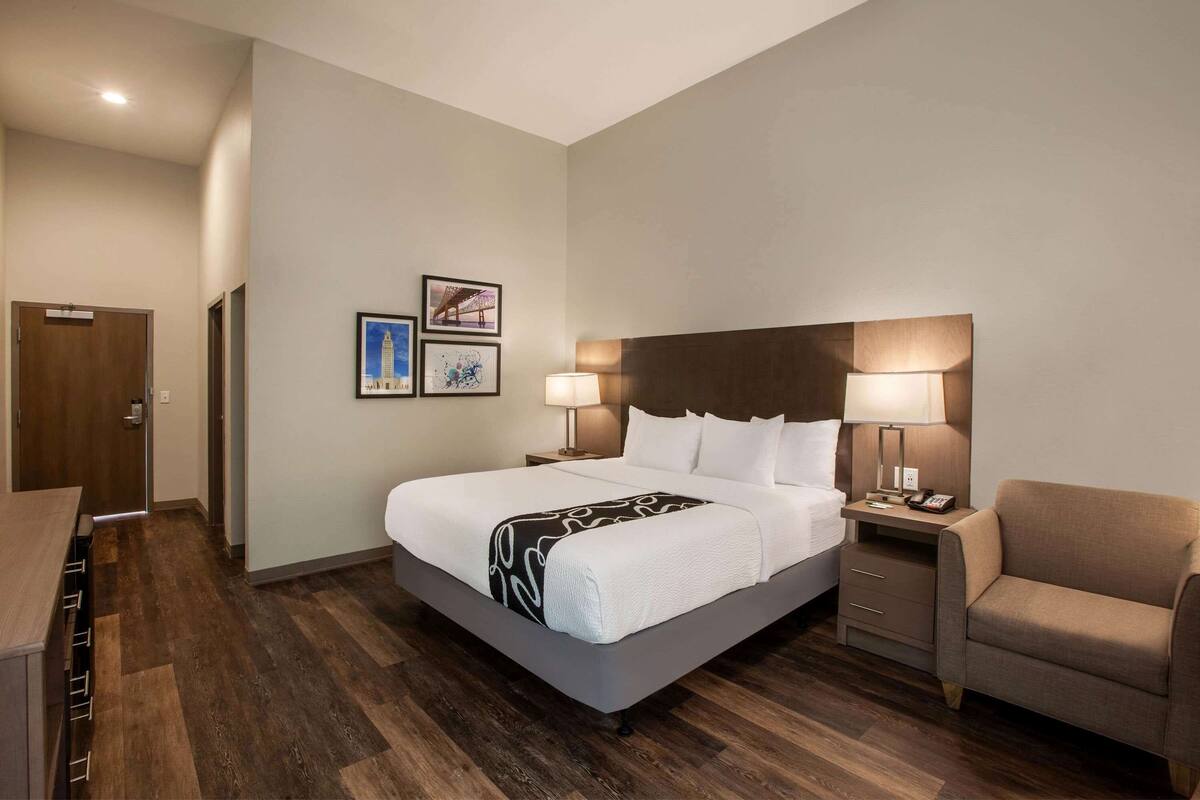 A hotel room with a large bed, bedside tables, a chair, and artwork on the wall.